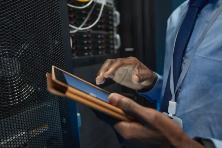 close-up-african-american-man-holding-digital-tablet-while-standing-by-server-cabinet-working-with-supercomputer-data-center-copy-space