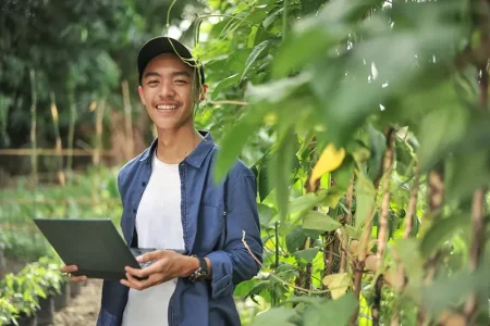 happy-young-asian-farmer-man-smiling-when-checking-long-beans-quality-using-laptop