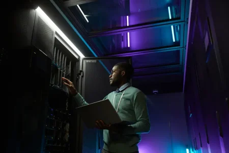 low-angle-portrait-young-african-american-data-engineer-working-with-supercomputer-server-room-lit-by-blue-light-holding-laptop-copy-space