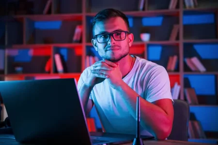 man-glasses-white-shirt-is-sitting-by-laptop-dark-room-with-neon-lighting